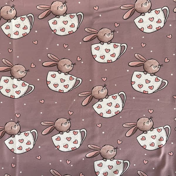 Altrosa Jersey-Stoff mit niedlichen Hasen in Tassen mit weißen Punkten und rosa Herzen im Hintergrund – ideal für süße Kinderkleidung wie Shirts, Kleider oder Pumphosen